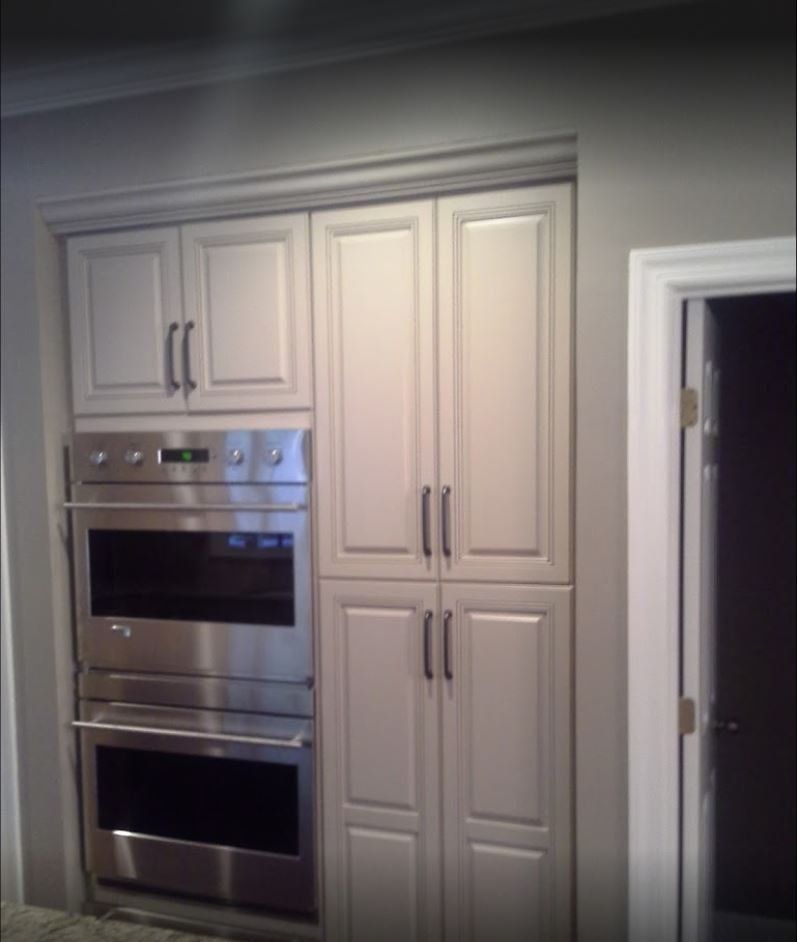 Built-in kitchen cabinets and oven in light color with dark handles next to a doorway.