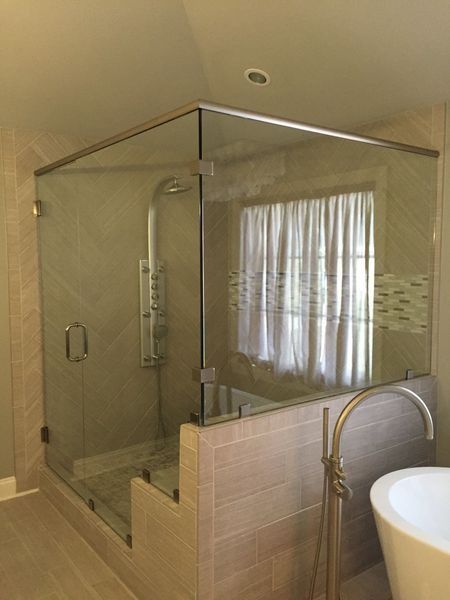 Glass shower enclosure in a bathroom with tiled walls, a tub, and shower fixture.