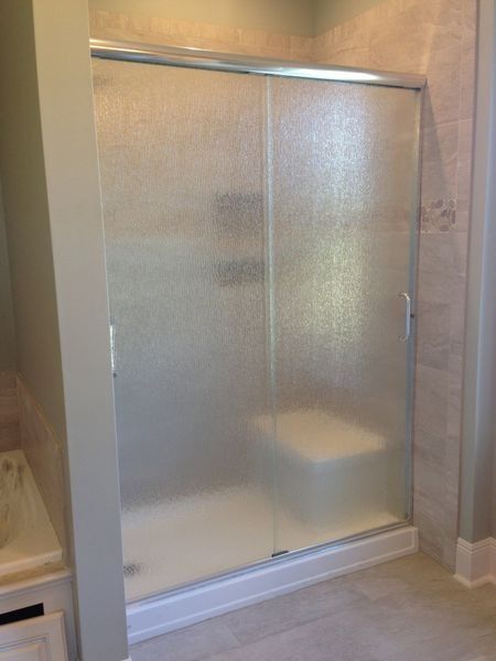 Frosted glass sliding shower doors with a white base and a built-in seat. Beige tile walls.