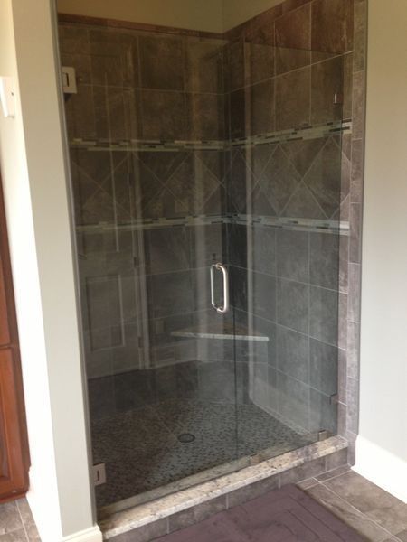 Glass shower enclosure with gray tile walls and a pebble floor.