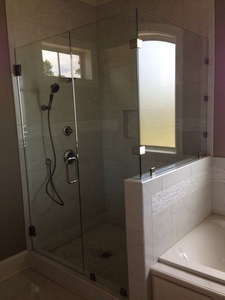 Glass shower enclosure with a window and a bathtub in a bathroom.