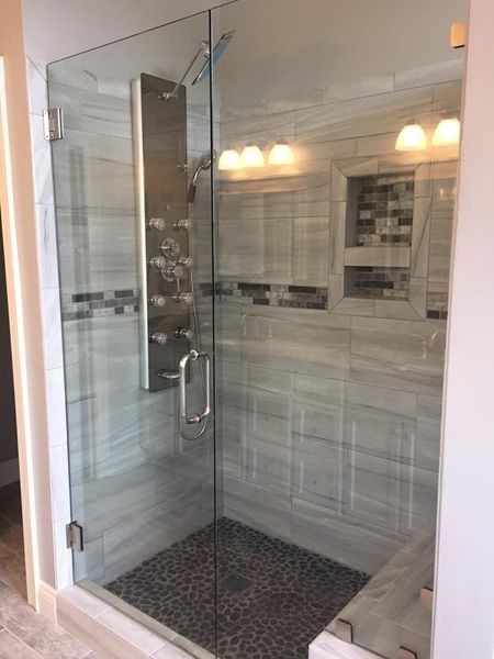 Modern glass shower with pebble floor, marble walls, and stainless steel shower panel.