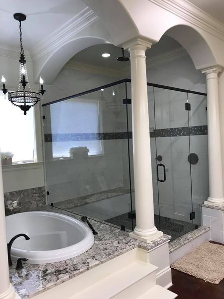 Elegant bathroom with a glass shower, jacuzzi tub, columns, and chandelier.
