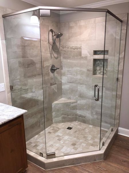 Glass-enclosed corner shower with beige tile and a built-in bench and shelf.