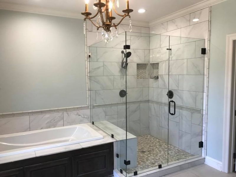 Bathroom with a glass-enclosed shower, bathtub, and marble tile. A chandelier hangs from the ceiling.