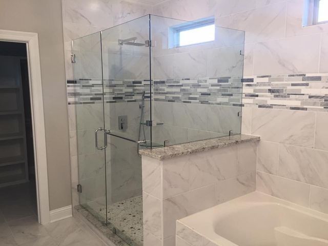 Glass shower enclosure in a bathroom with marble tile and a tub.