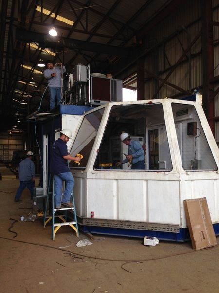 Workers assembling a white and blue industrial structure inside a large warehouse; some are using tools.