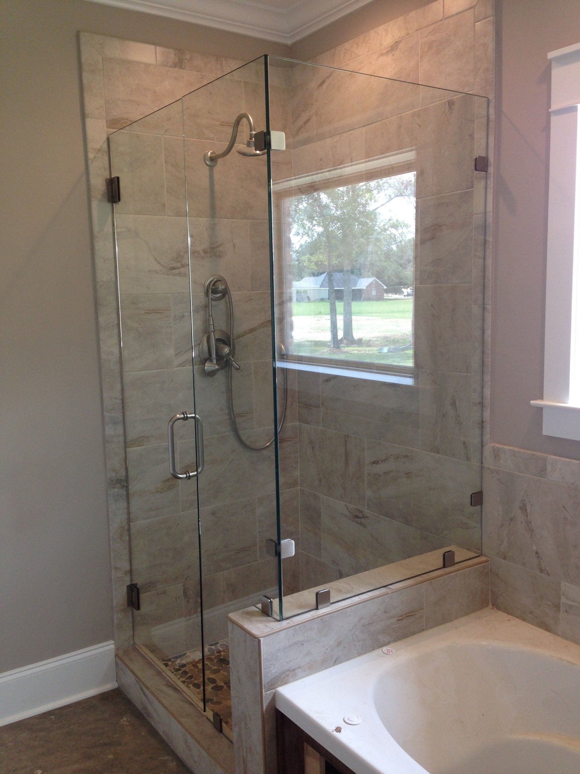 Glass shower enclosure in a bathroom with beige tile, beside a bathtub.