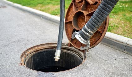 A sewer cover is open and a hose is coming out of it.