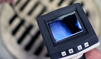 A person is holding a camera over a drain.