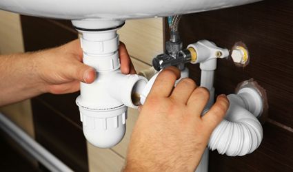 A man is fixing a sink pipe in a bathroom.