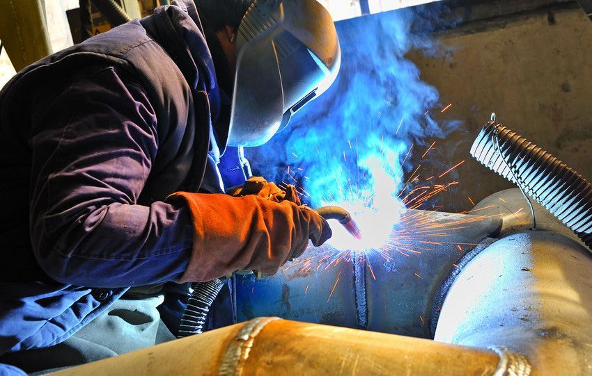 A man wearing a welding mask is welding a piece of metal.