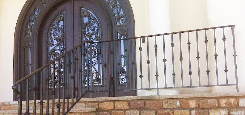 A wrought iron railing with stairs leading up to a door.