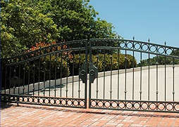 A wrought iron gate is sitting on top of a brick driveway.