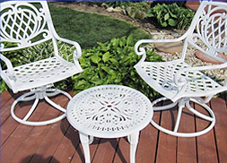 Two white chairs and a white table are on a wooden deck.