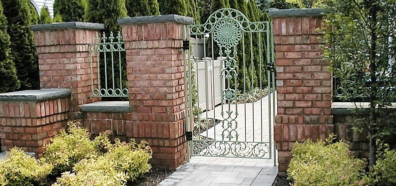 A brick wall with a wrought iron gate leading to a garden.