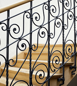 A close up of a wrought iron railing on a set of wooden stairs.