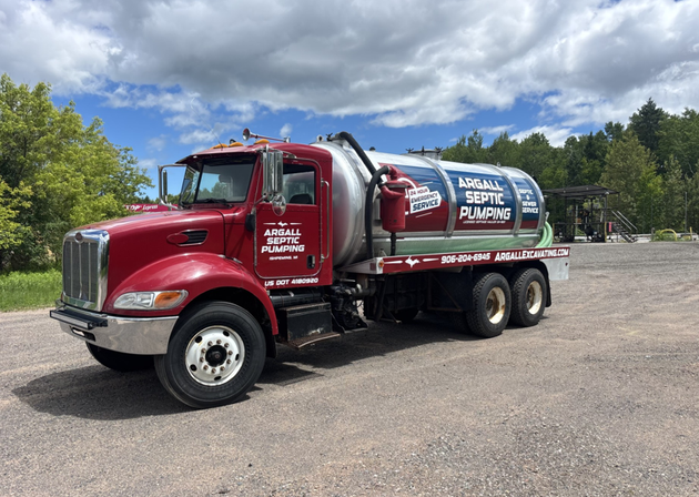 Red septic service truck parked on a gravel lot under a cloudy sky