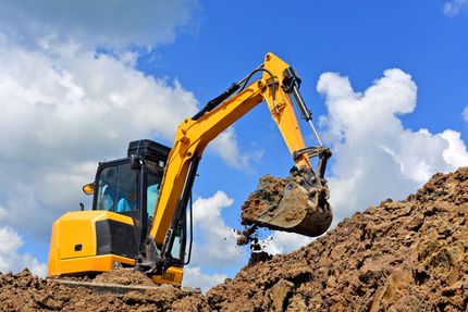 Yellow excavator digging dirt under a blue sky with clouds