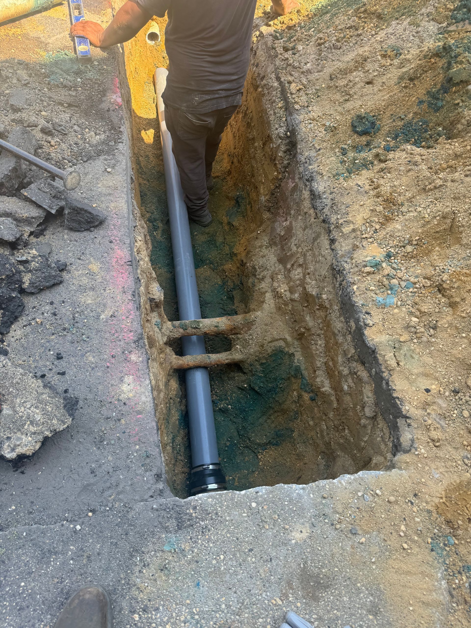 Man in trench installing a pipe. The trench is in the ground next to a road.