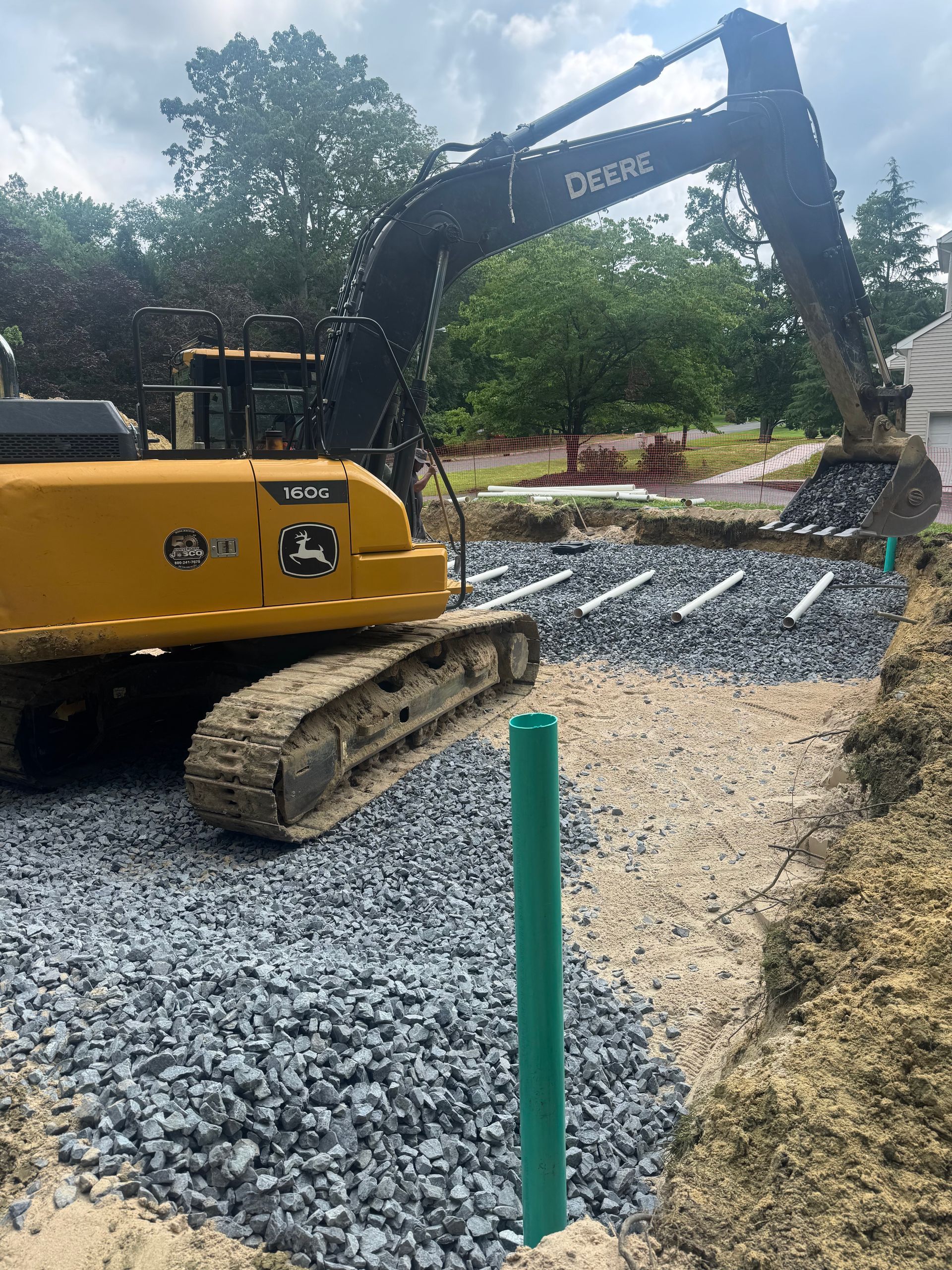 A John Deere excavator working on a gravel-lined trench with drainage pipes; outdoors.
