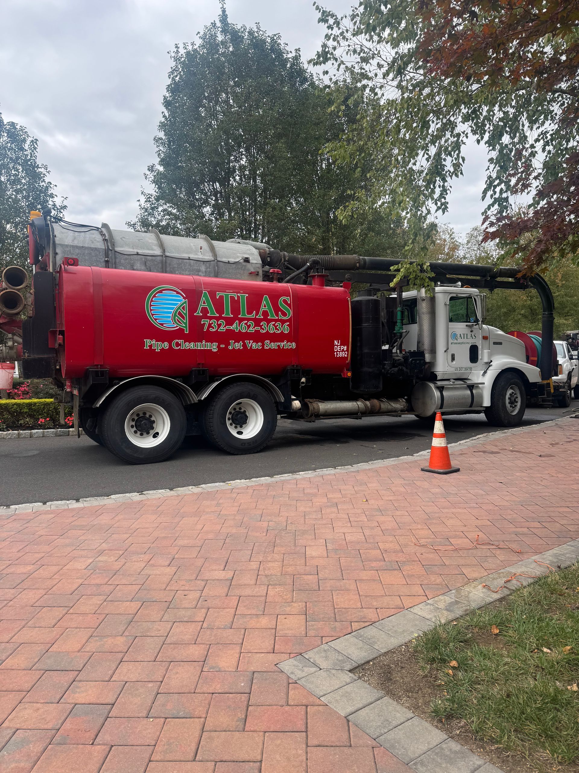 Red Atlas truck parked on a brick road with an orange cone, green trees in background.