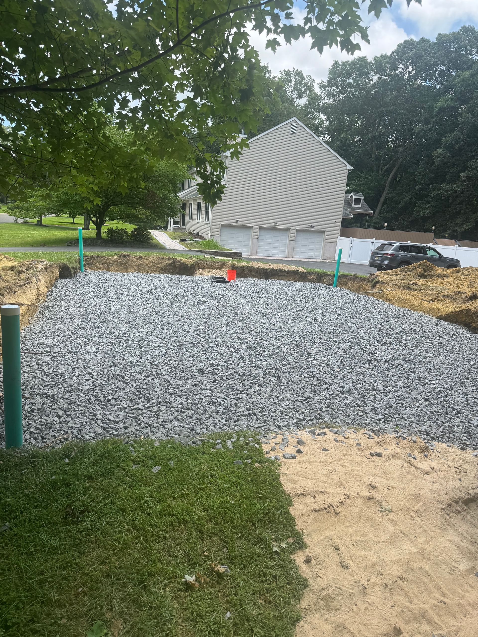 Gravel-filled area with green pipes, possibly a septic system, in front of a house.
