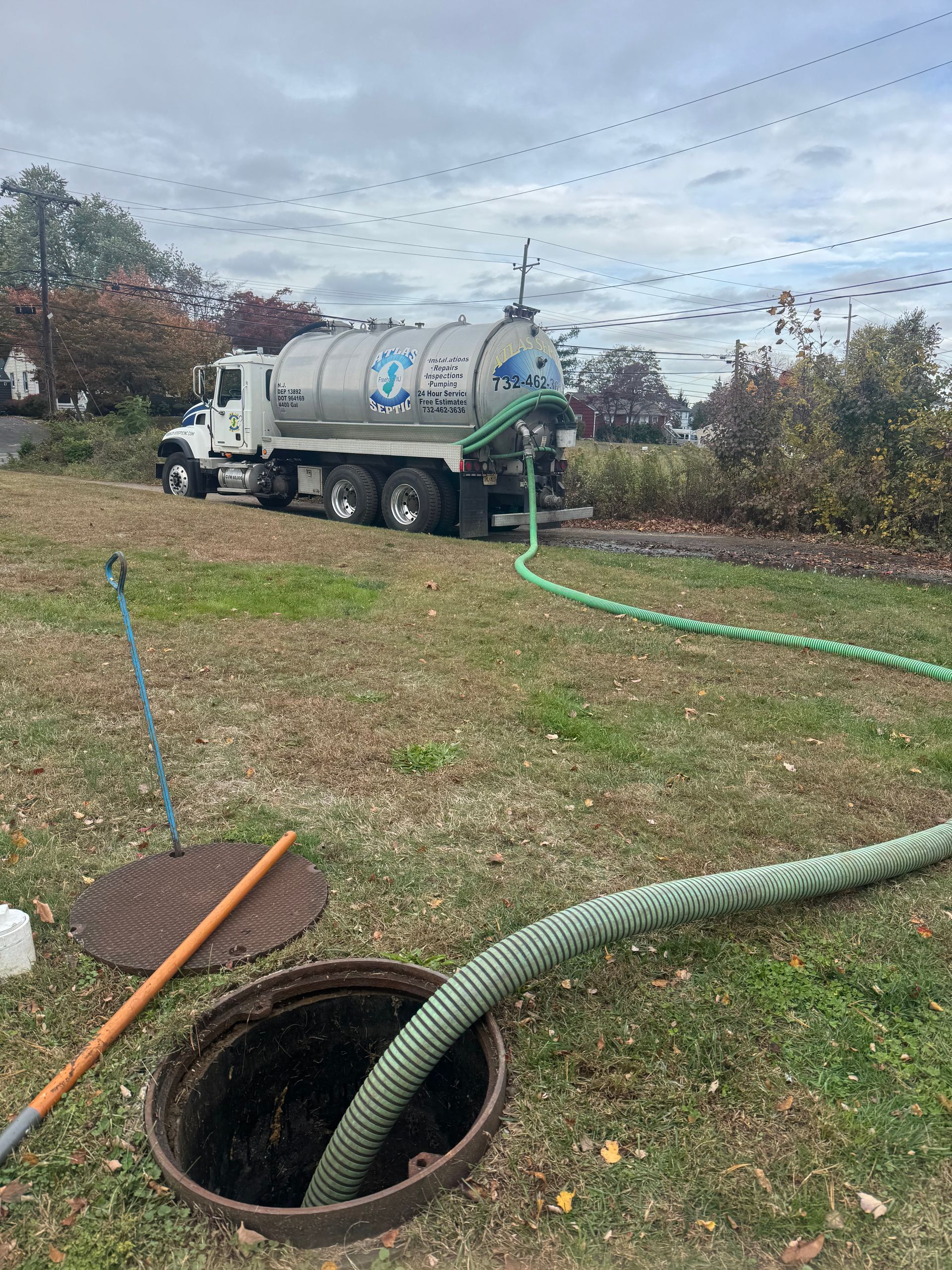 Septic tank service truck pumping sewage from an open manhole on a grassy lawn.
