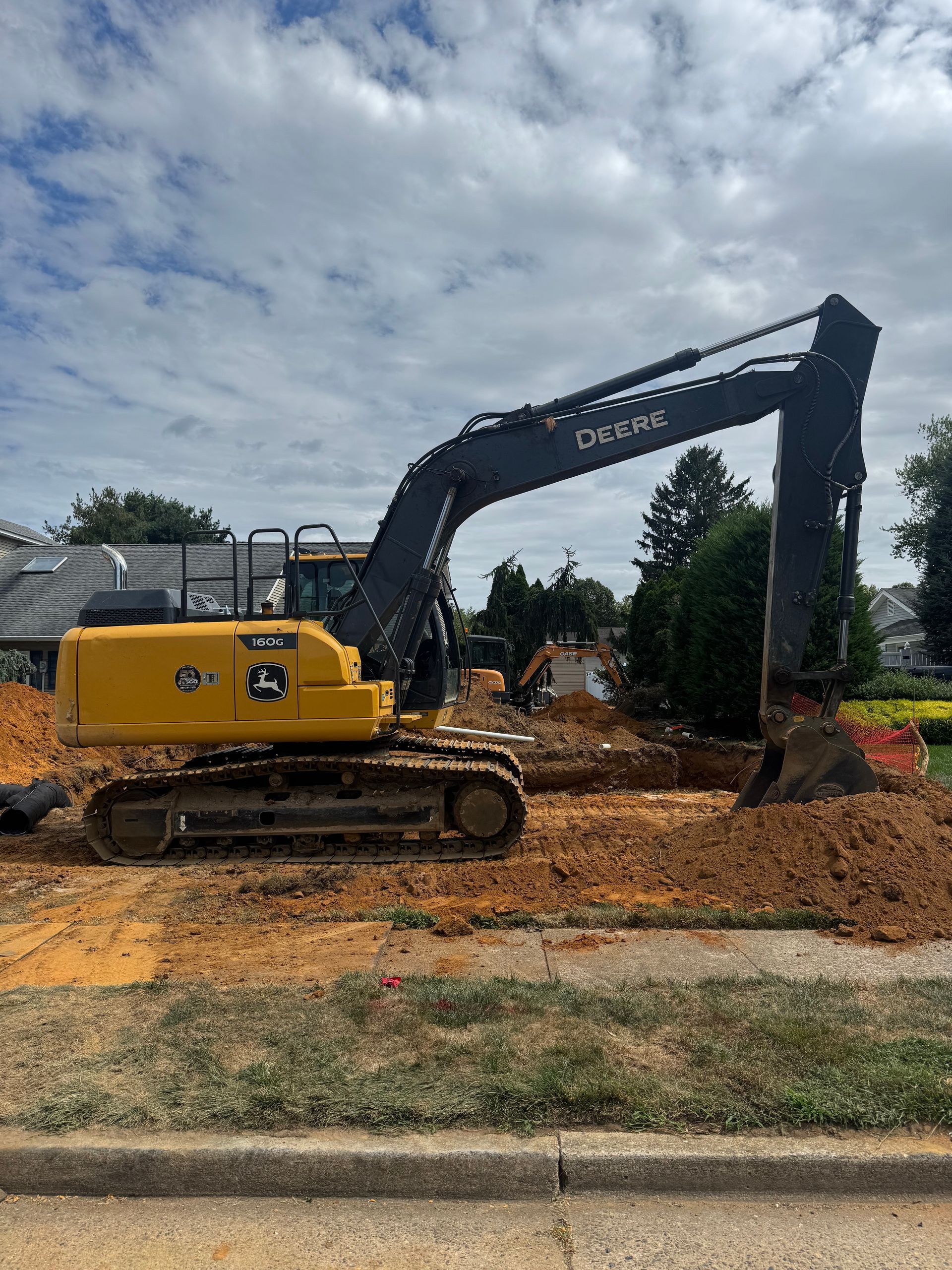 Yellow excavator digging in a dirt area near a road, under a cloudy blue sky.