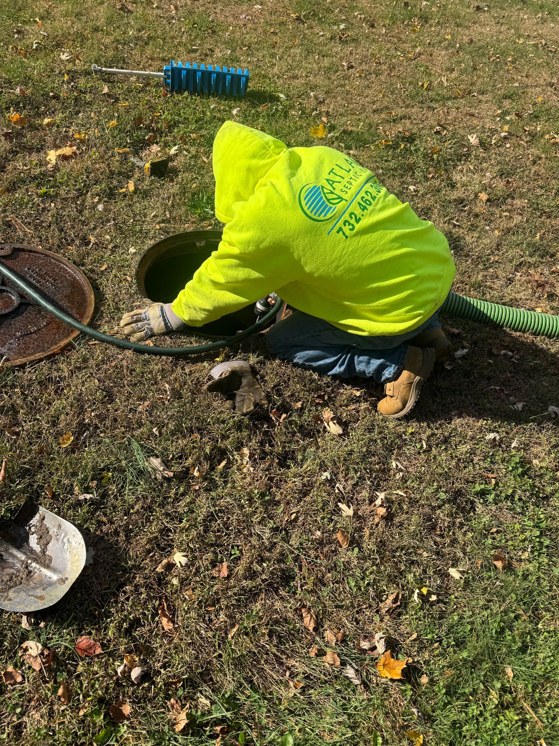 Person in a neon yellow jacket working at an open septic tank on a grassy lawn.