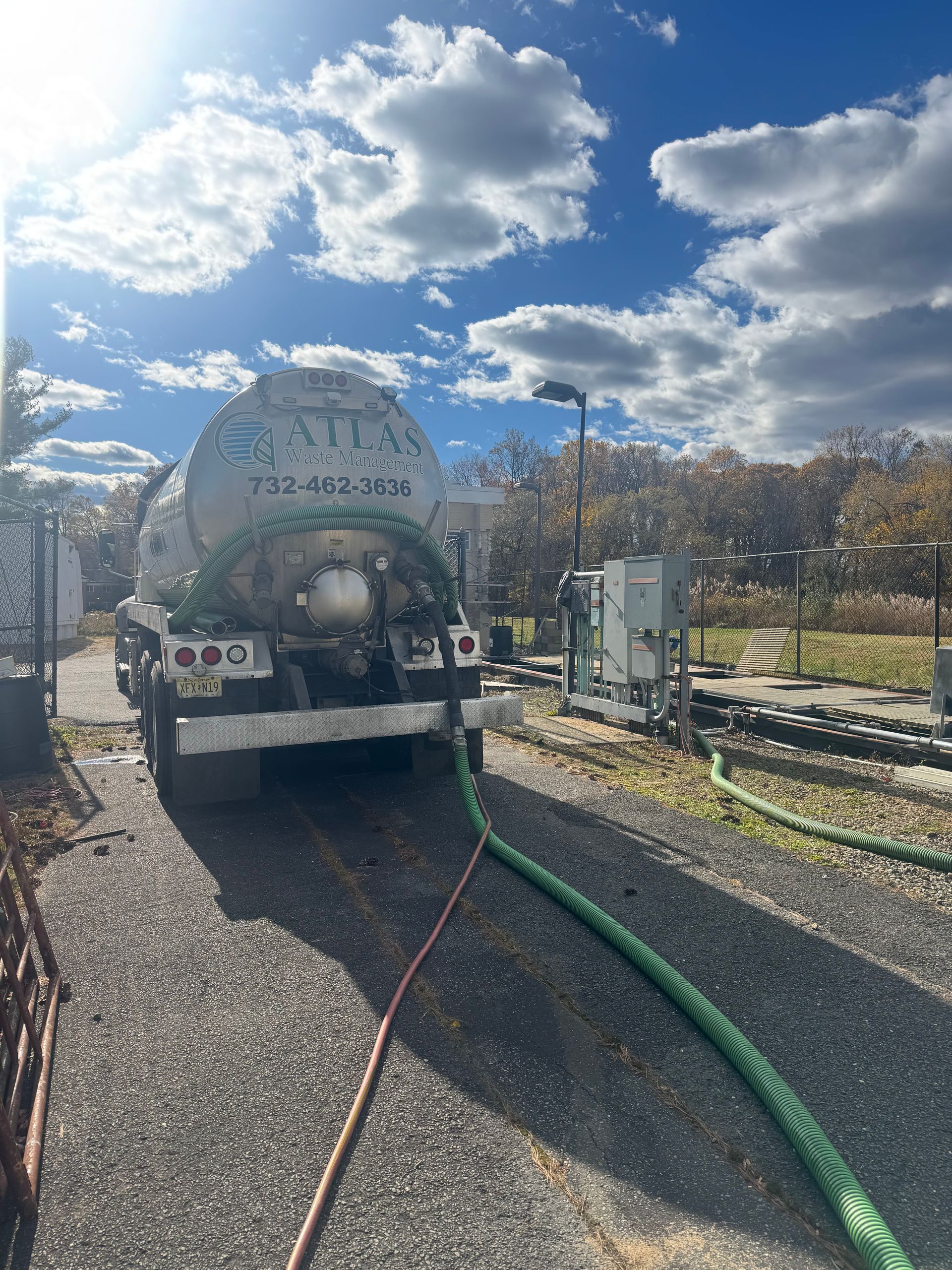 Tanker truck pumping waste from a septic system, green hose, gravel driveway, cloudy sky.