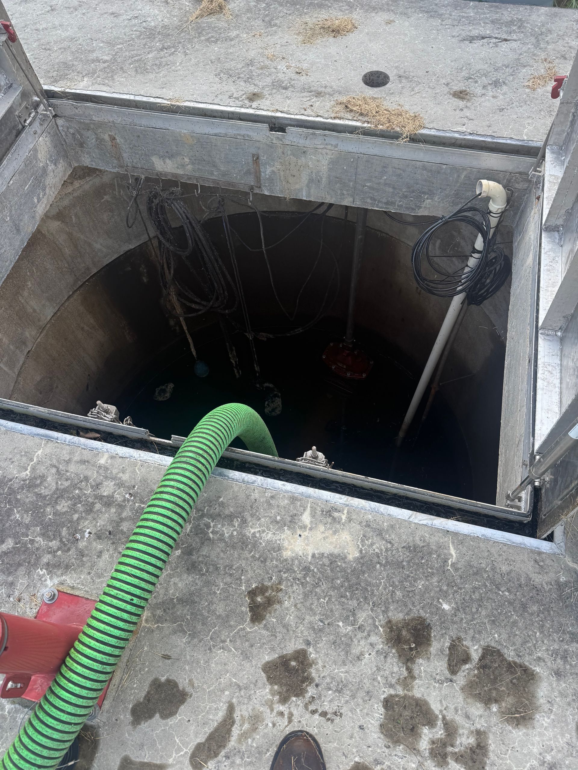 Open concrete manhole with green hose inside and a net.