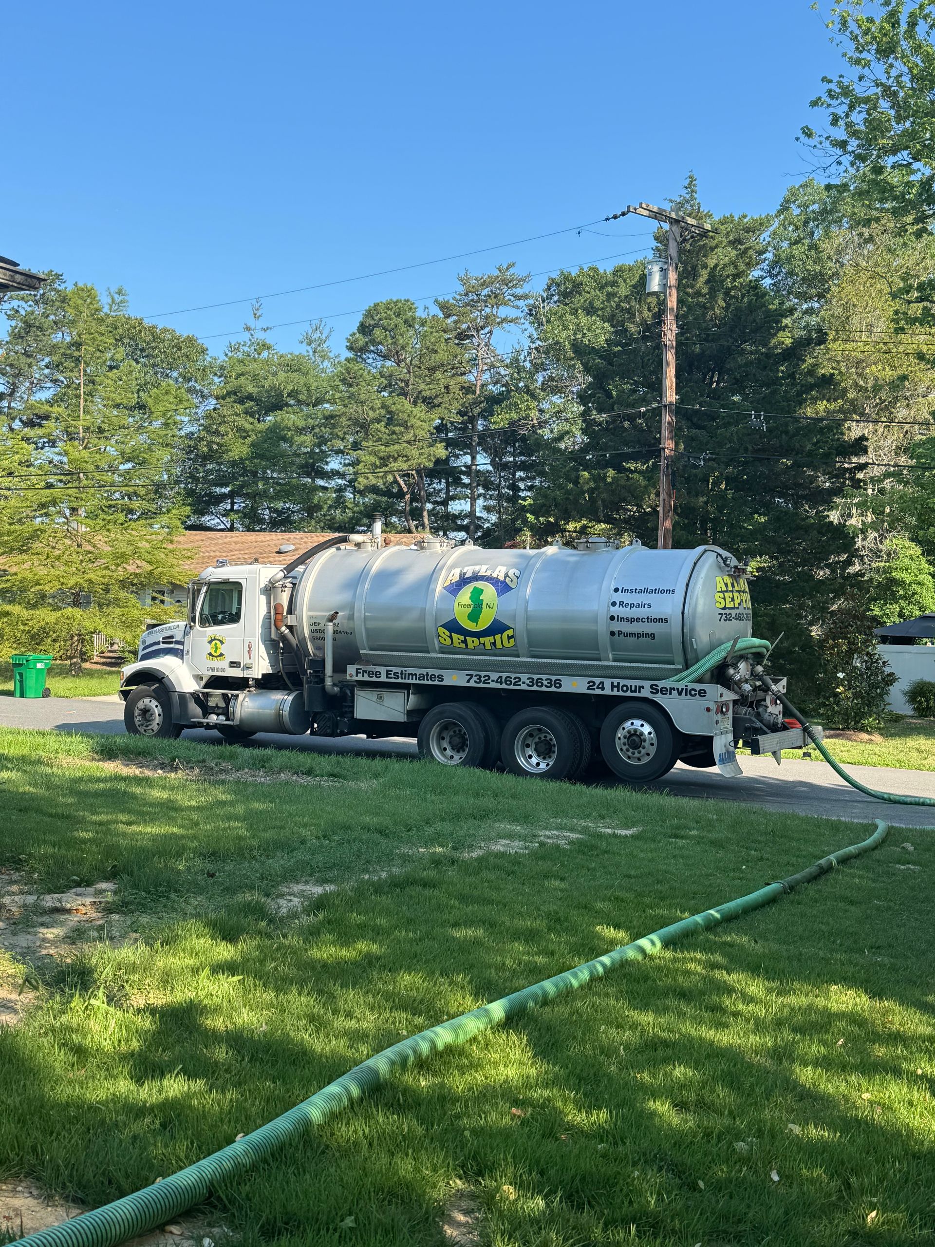 Septic tank truck parked on a residential street with a hose extended towards an unseen location.