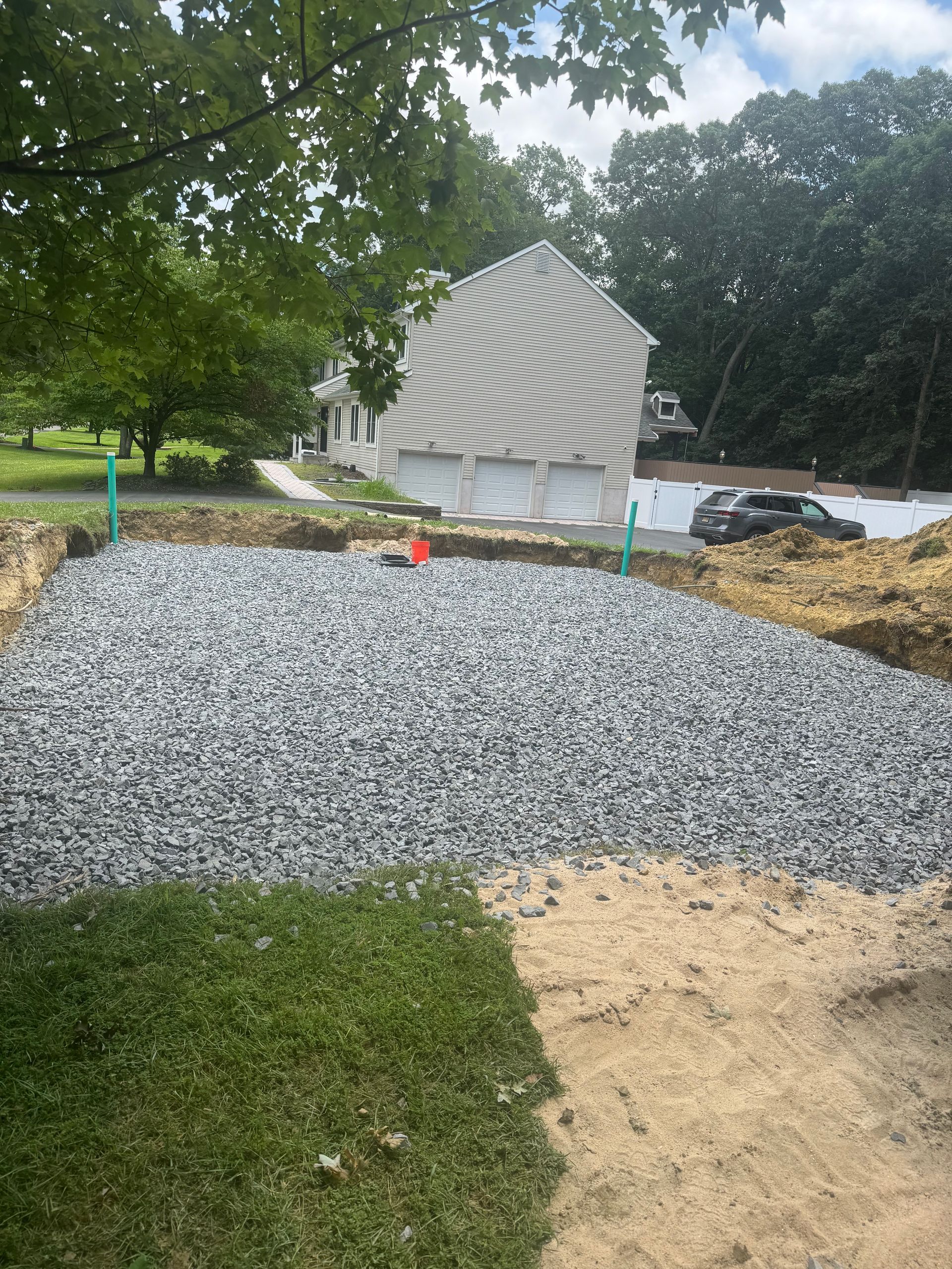 Gravel-filled rectangular area, likely for a septic system, in front of a house with garage doors. Green pipes present.