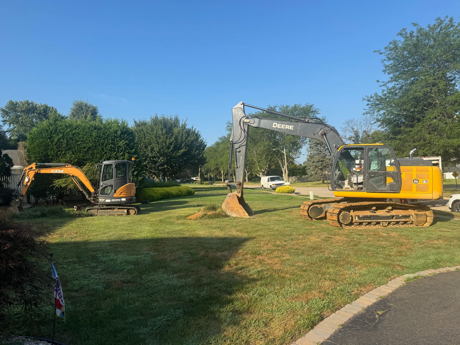 Three excavators on a grassy lawn under a clear blue sky.