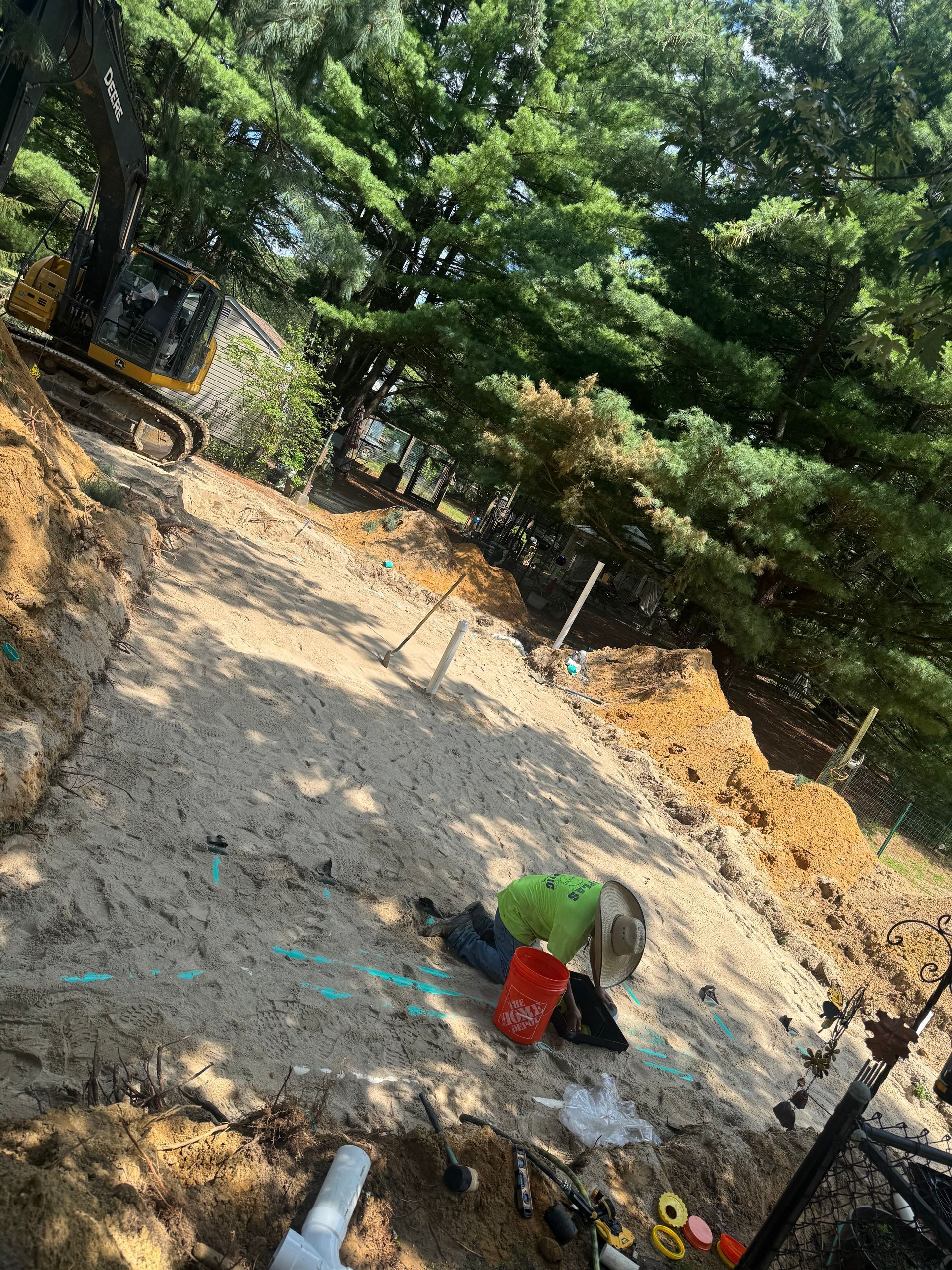 Construction site with excavator on a hillside; worker in green shirt, and a bucket.