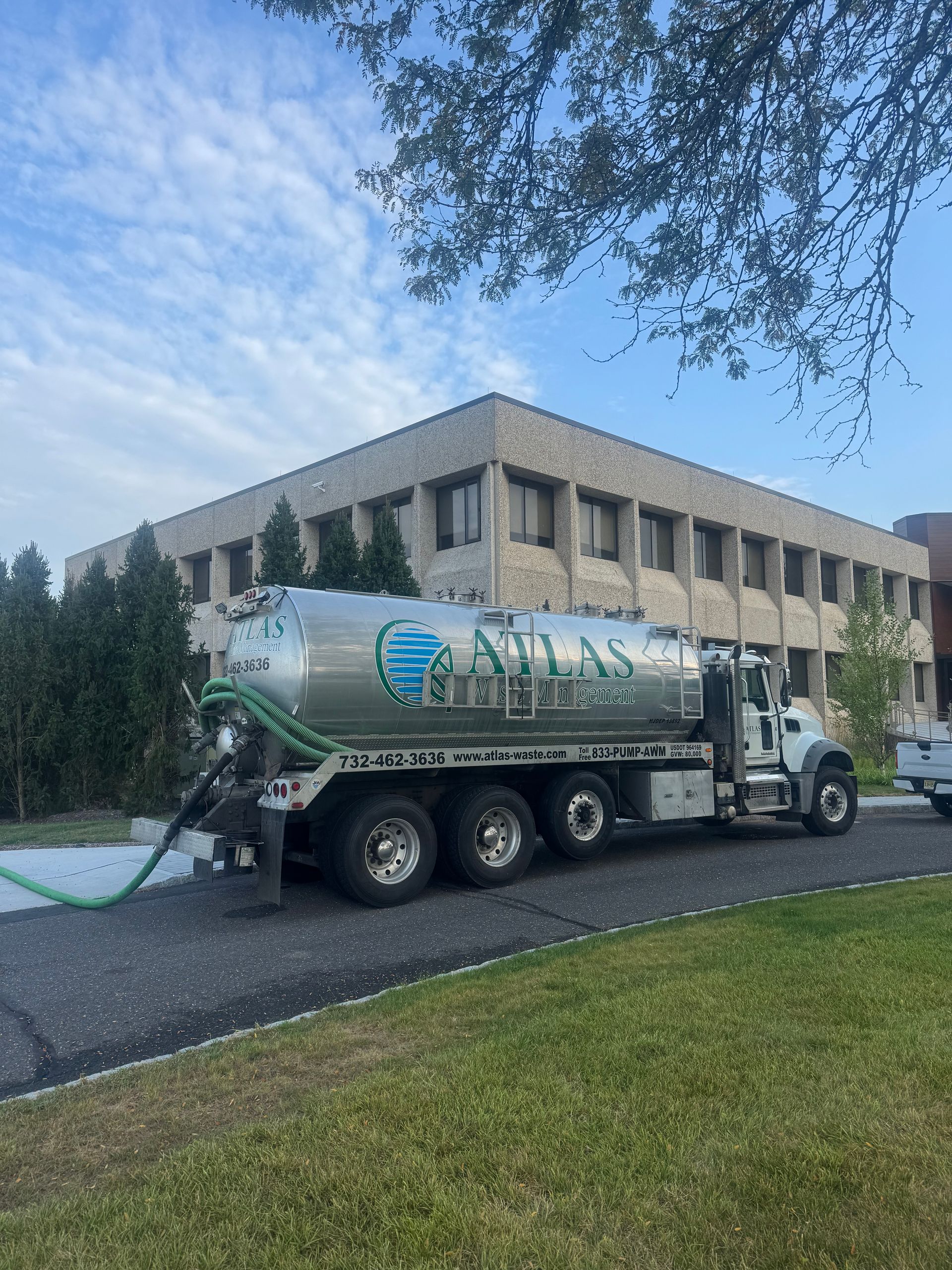 Septic truck parked in front of a building; a green hose extends from the truck.