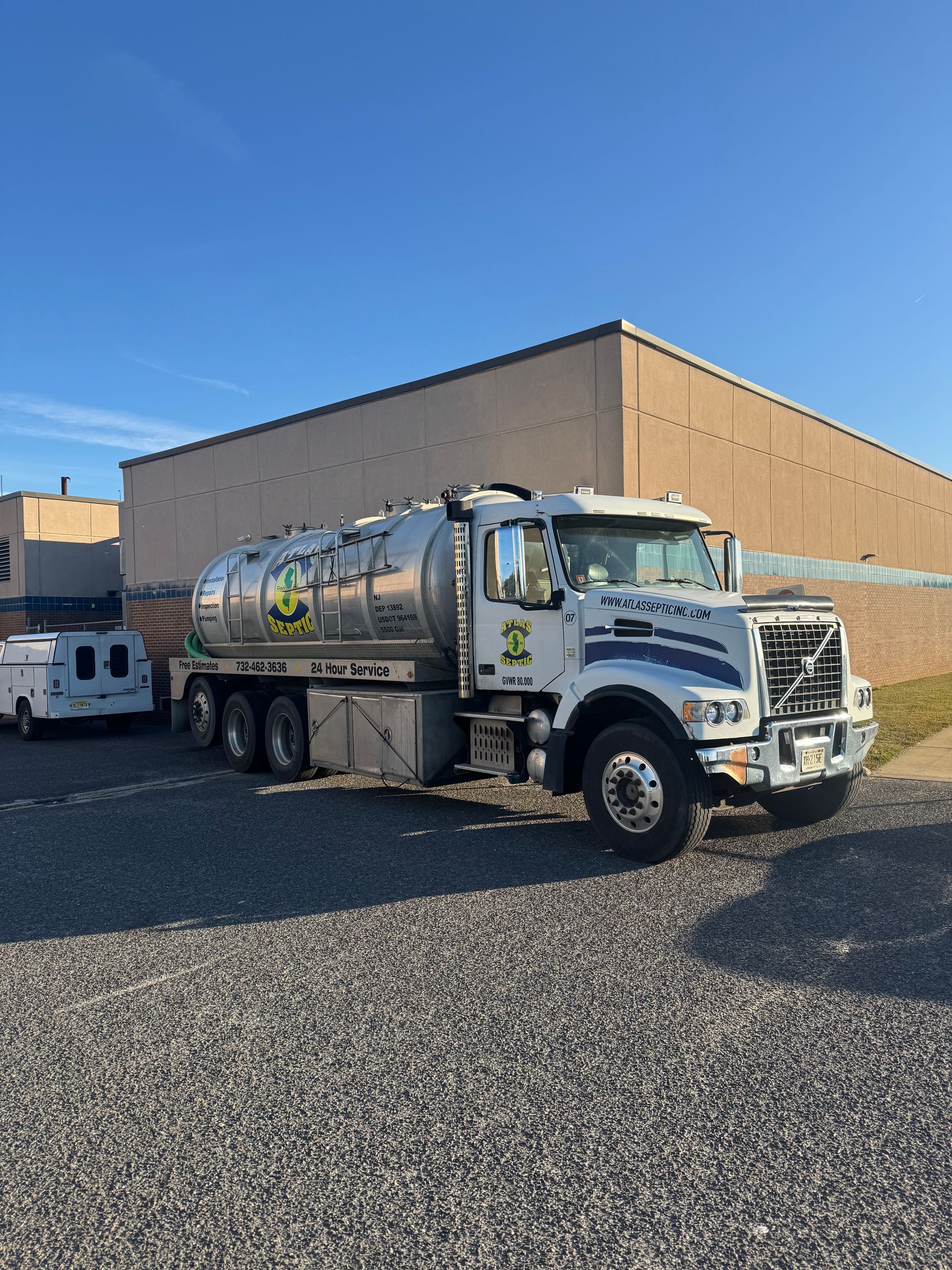 White tanker truck parked on gravel in front of a tan building. Clear blue sky.