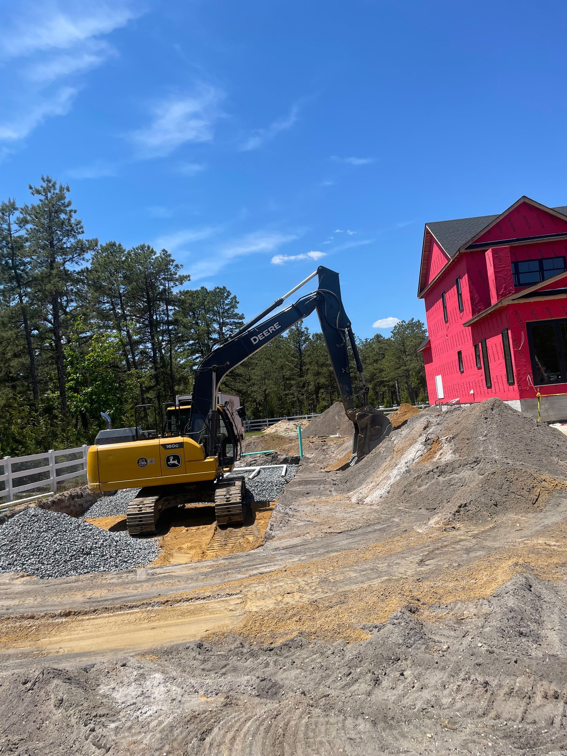 Excavator digging near a partially built red house on a construction site; blue sky.