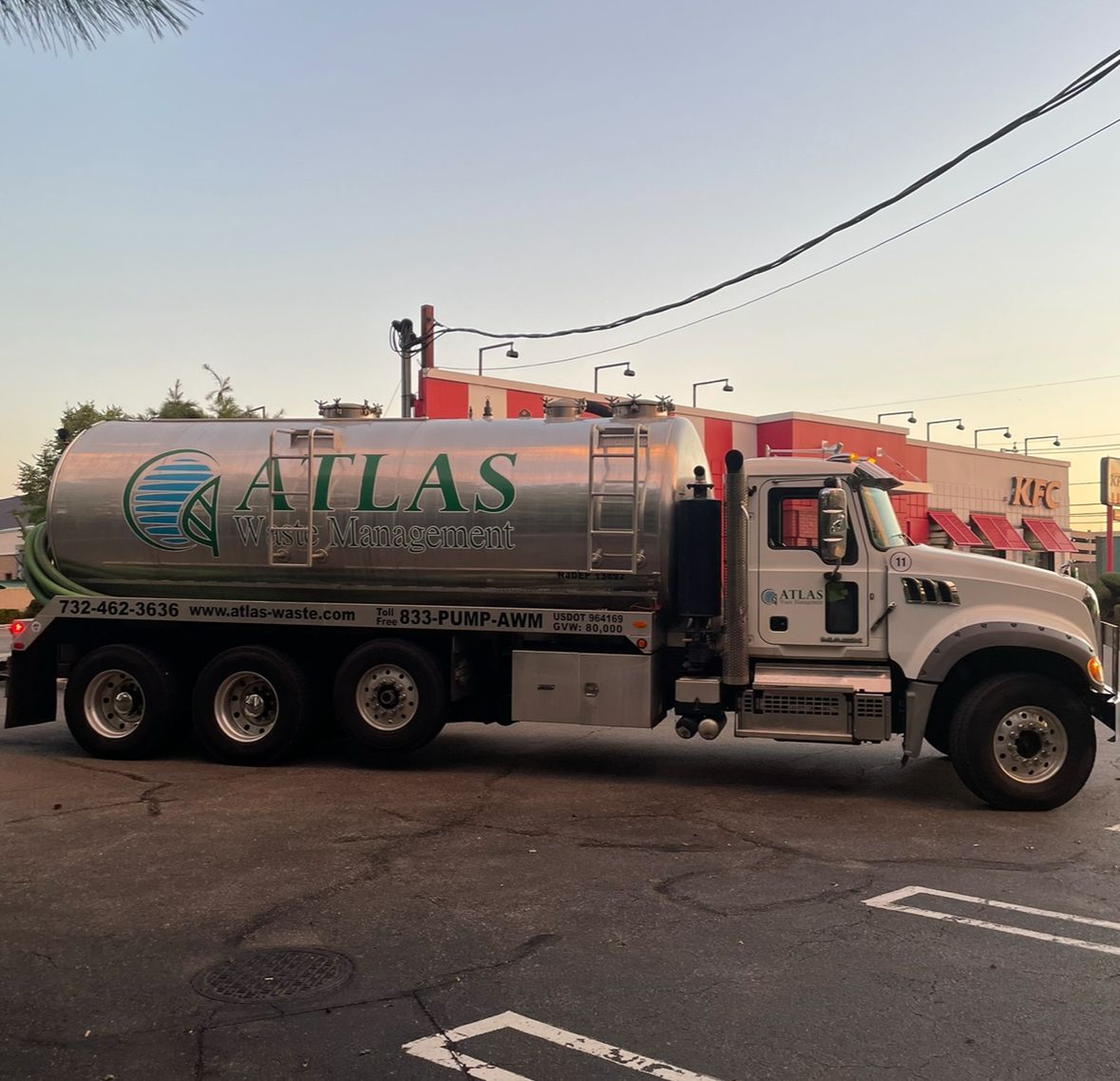 A silver Atlas Sanitation truck parked on a paved lot with a building in the background.