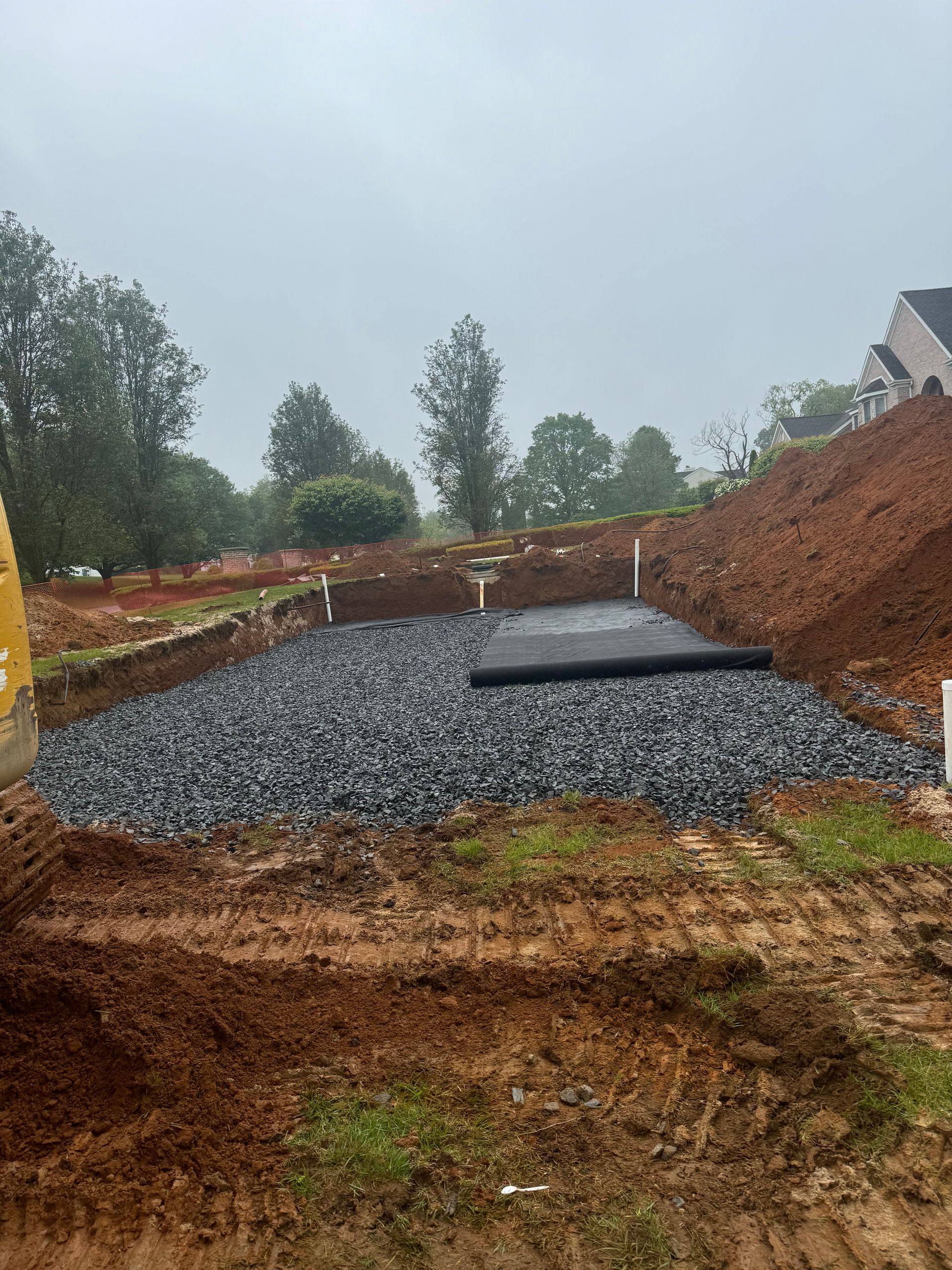 Excavation site with a gravel-filled area, drainage pipes, and a black fabric cover.