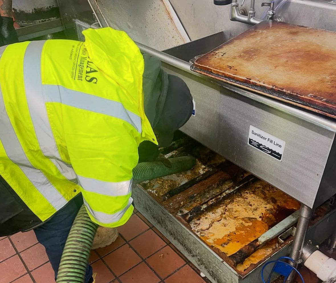 Person in yellow jacket cleaning a greasy kitchen sink with a hose.