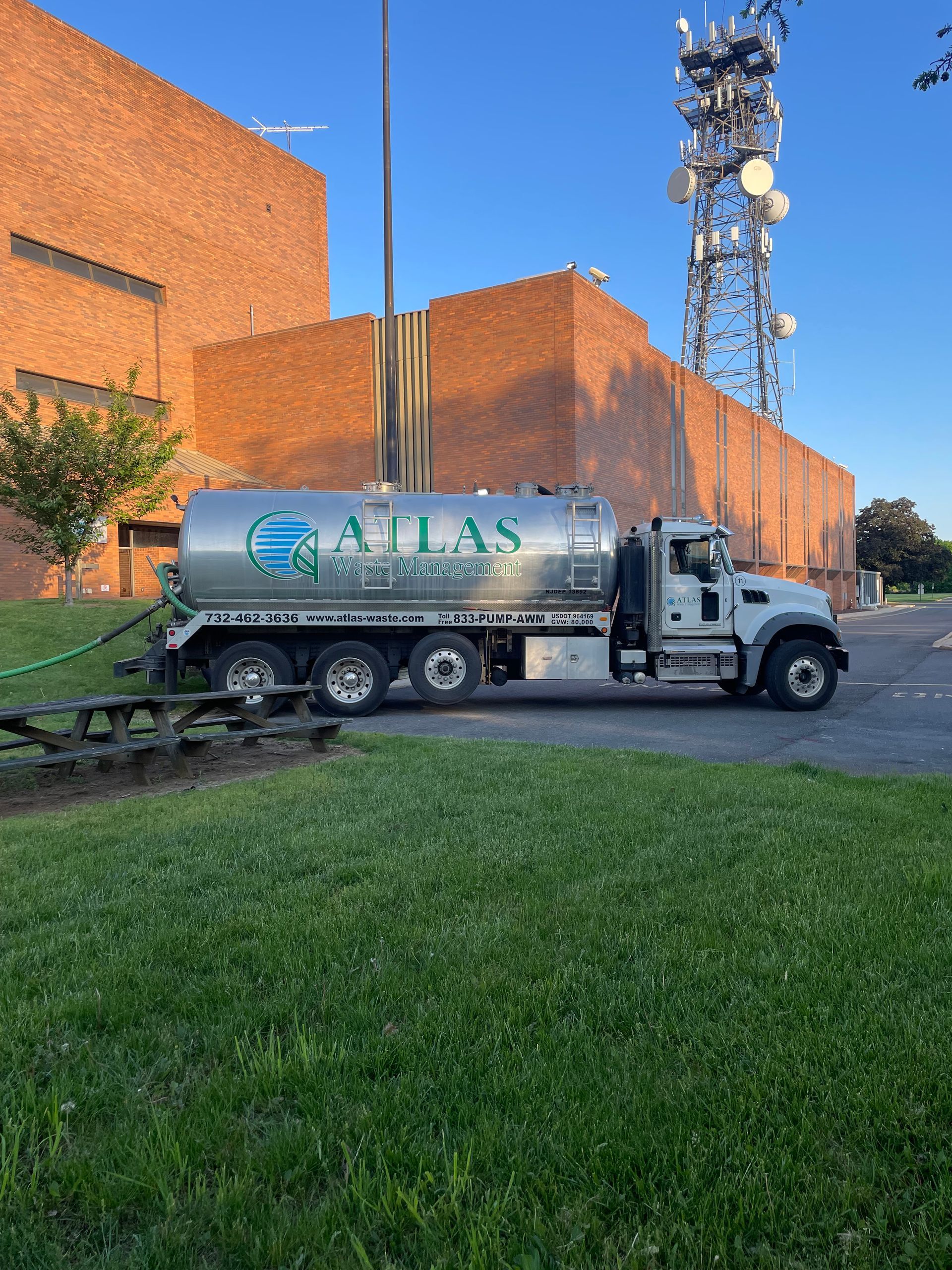Atlas Septic Services truck parked by a brick building and a communications tower, with green grass in the foreground.