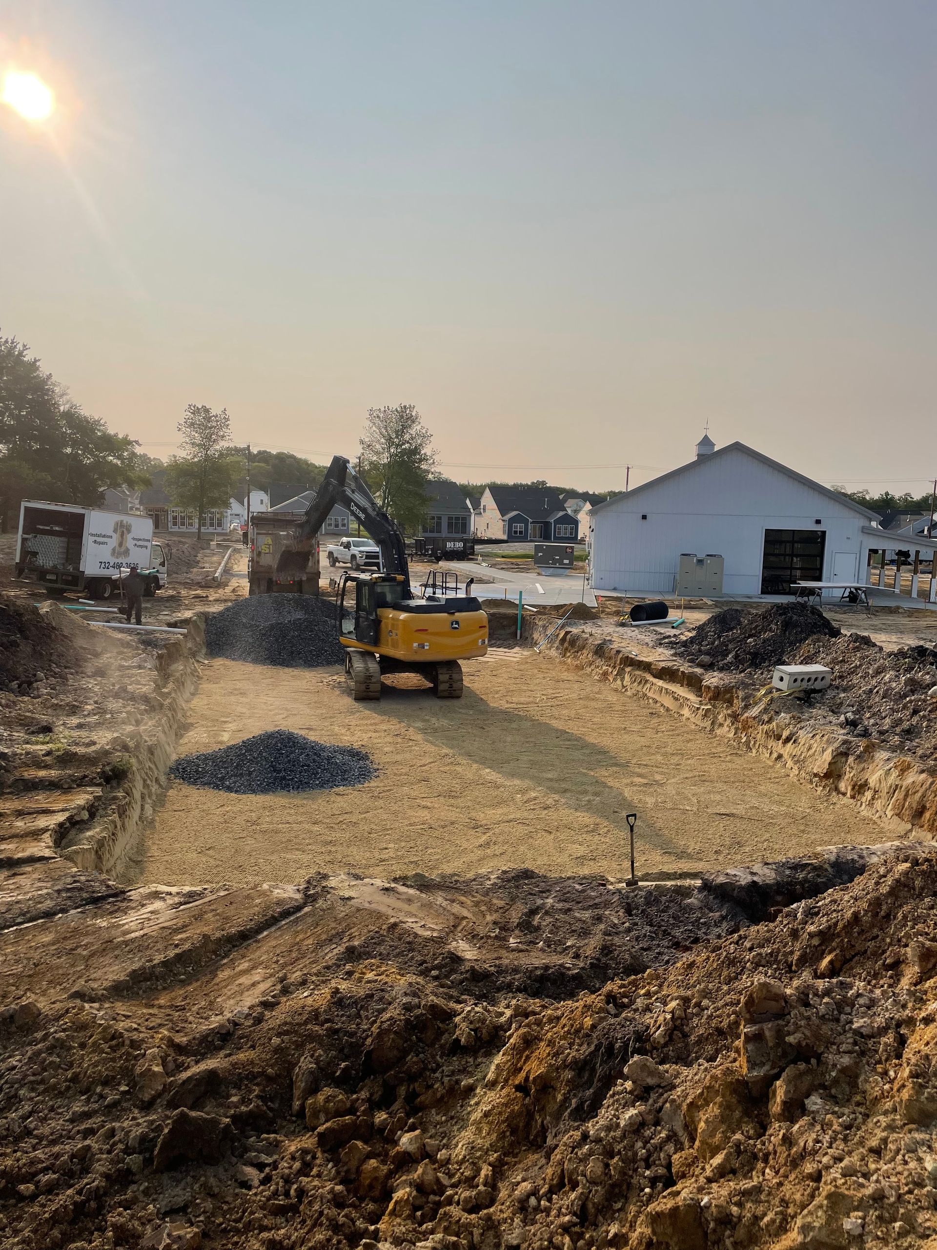 Construction site with a yellow excavator removing gravel. A partially built white building is in the background.
