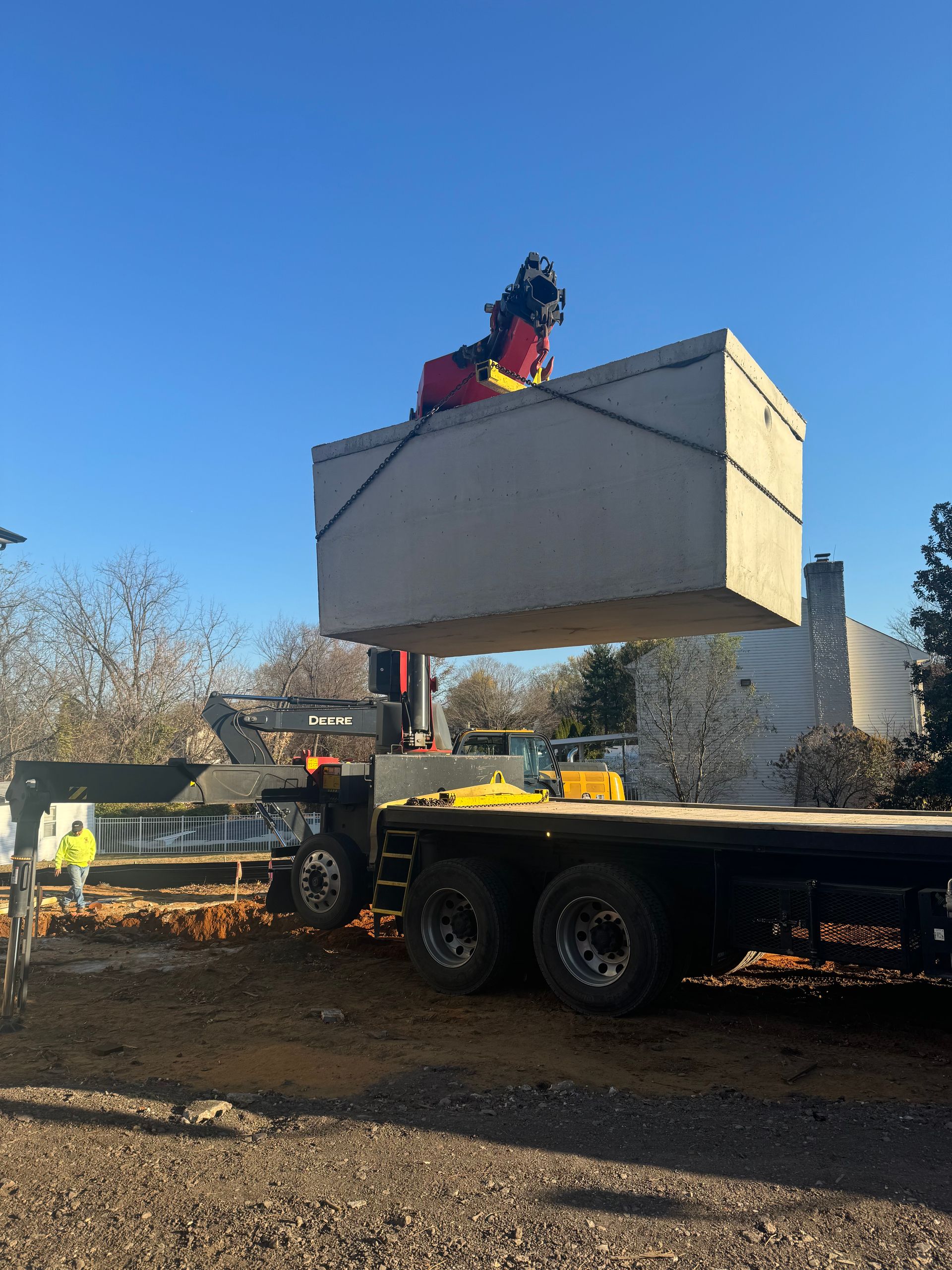A crane lifting a large concrete box from a flatbed truck on a construction site. Clear, blue sky.