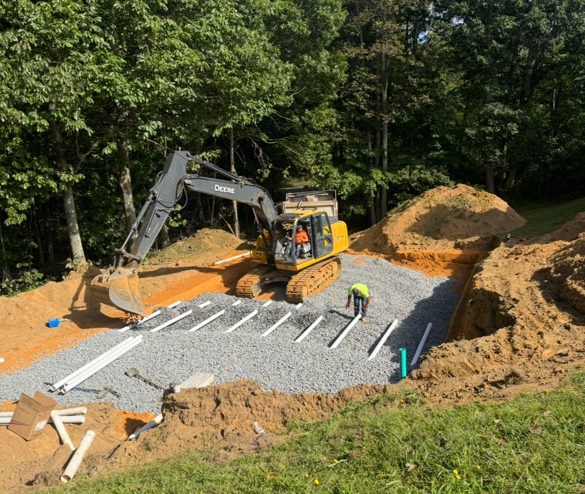 Construction site with excavator and worker installing septic system pipes.