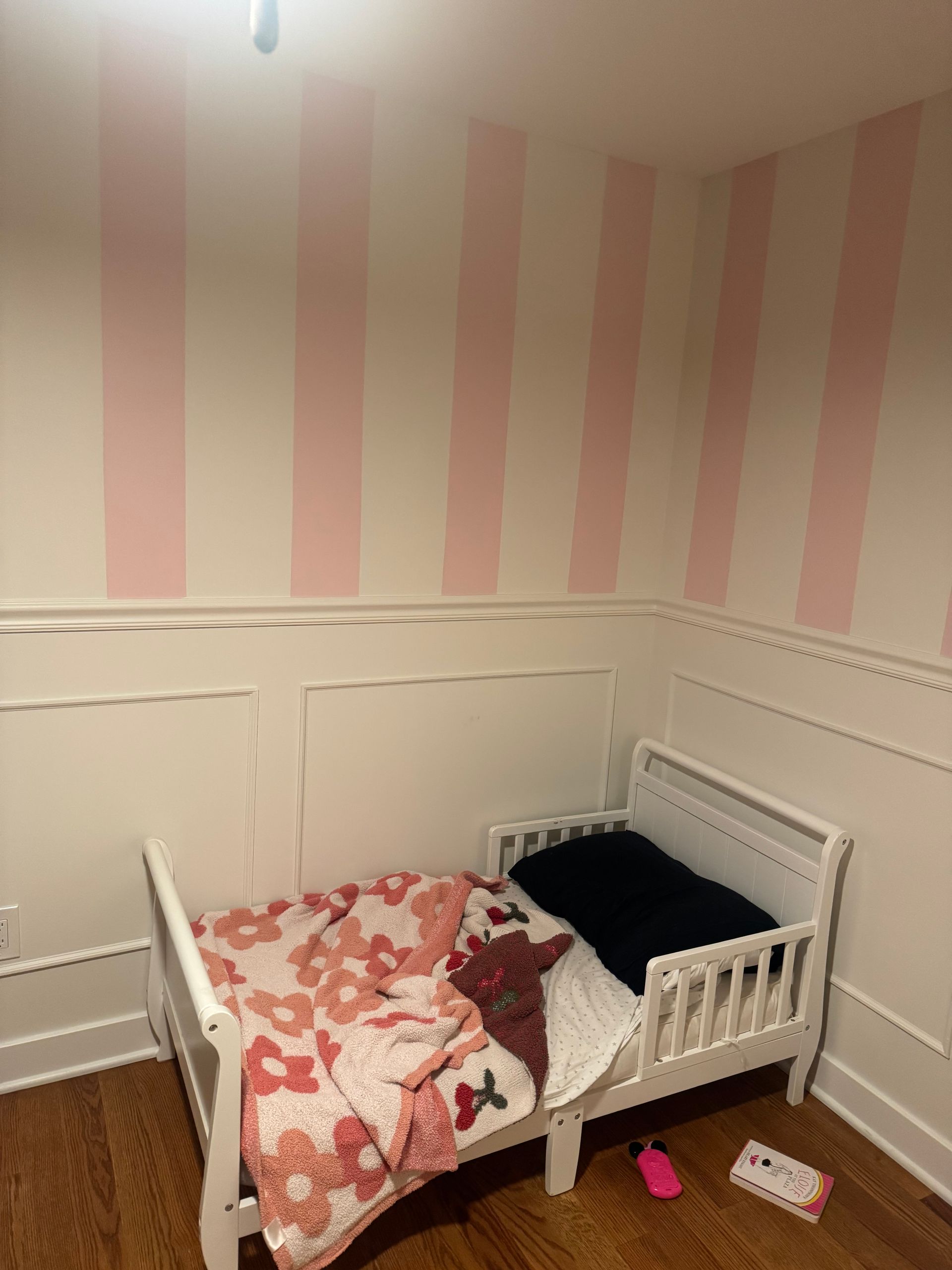Child's white bed in a room with pink and white striped walls, blanket, and pillow.