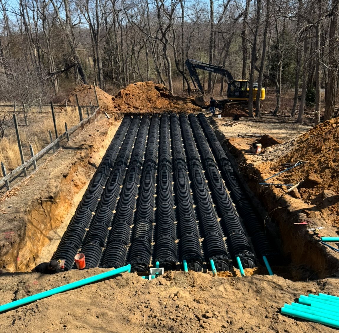 Excavated area with rows of black plastic septic chambers and blue PVC pipes, construction site.