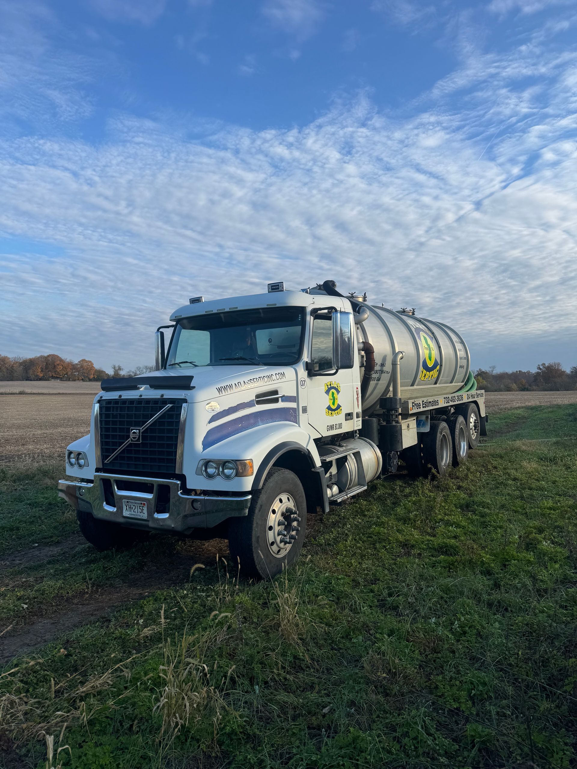 White Volvo truck with tank on field under cloudy sky.