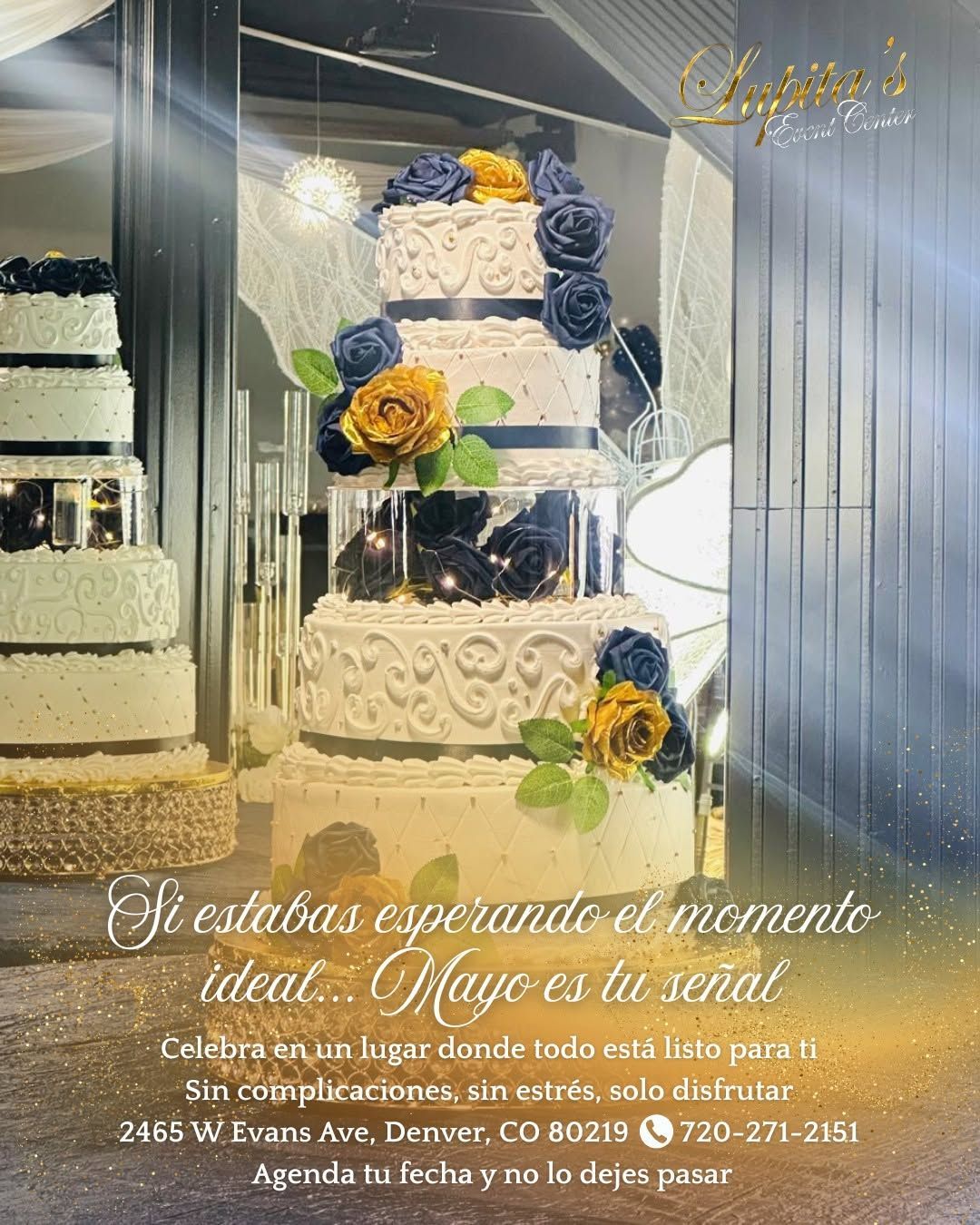 Three-tier white wedding cake with blue and yellow flowers in a reflective display case.